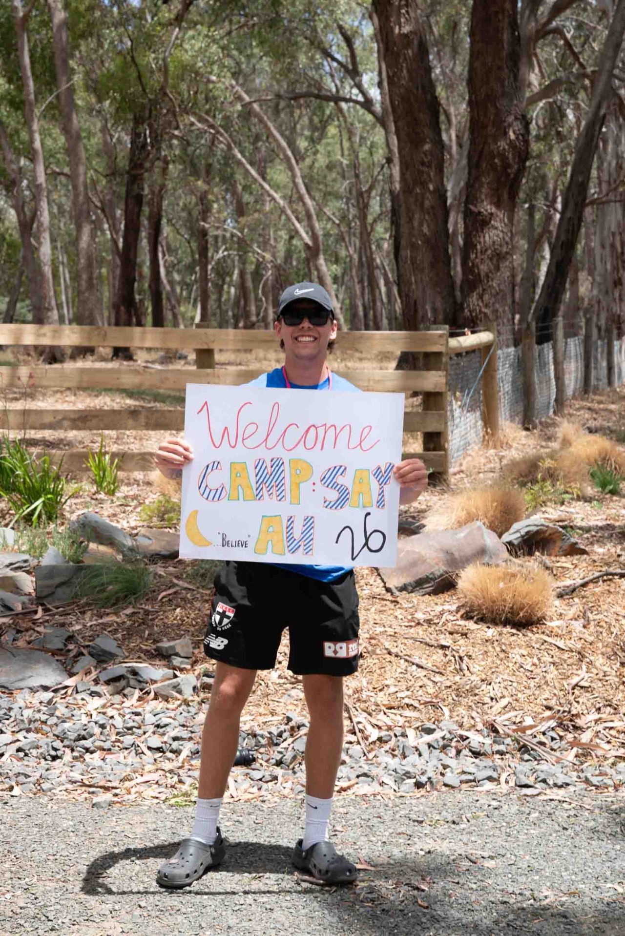 Person holding 'welcome to camp say' sign