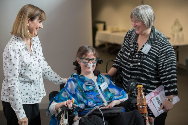 Three women smiling, one woman in a wheelchair smiling while using a ventilator machine