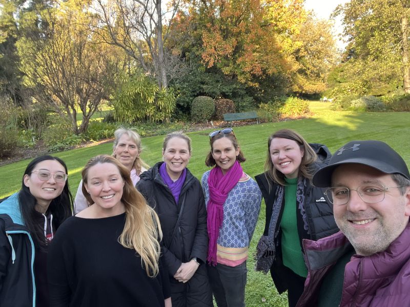 Seven people stand in a group outdoors, smiling at the camera