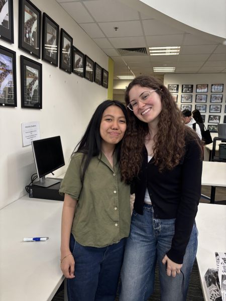 Two people stand indoors together smiling at the camera